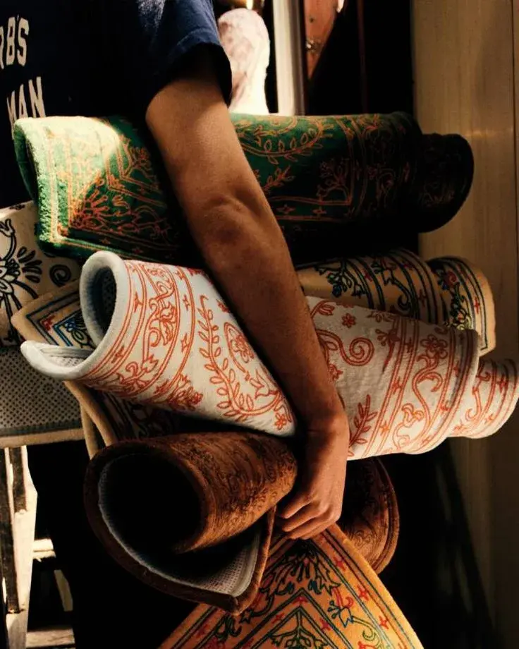 An arm carrying several rolled, richly patterned rugs