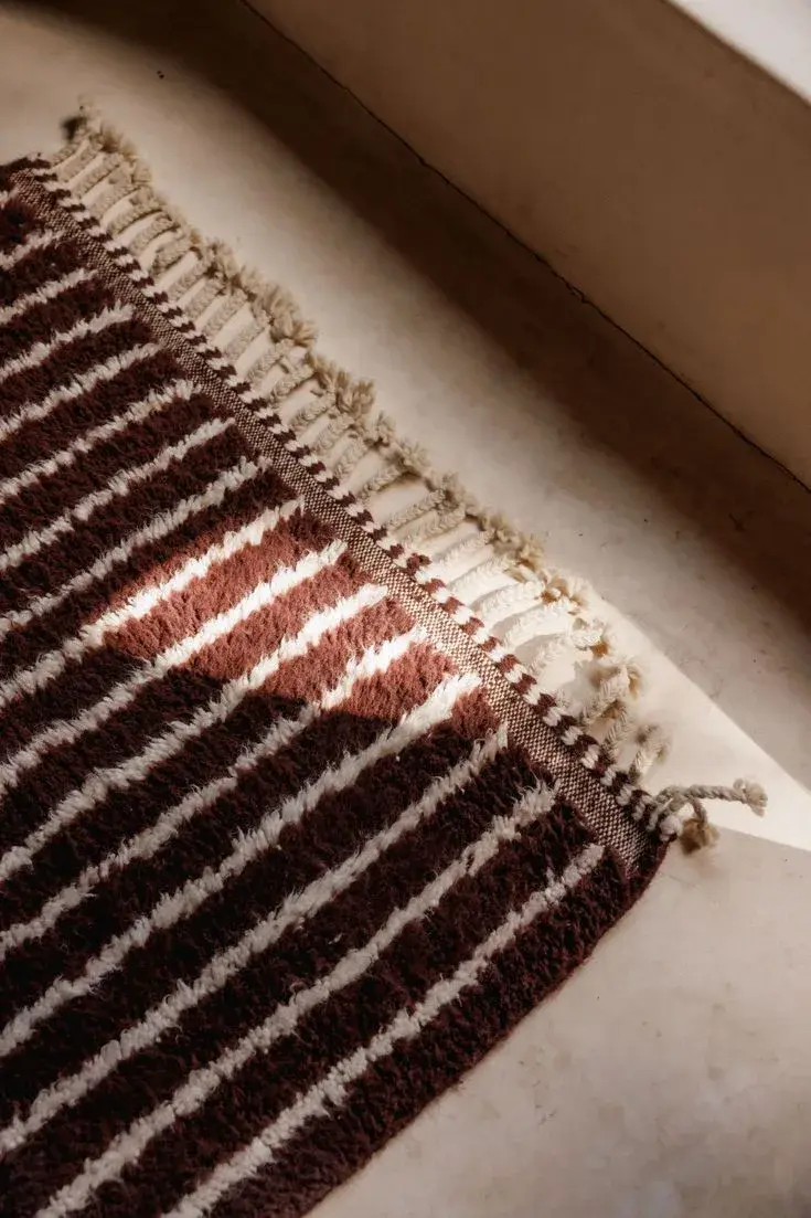 A brown and cream striped pile rug with knotted fringe, lit by afternoon sun