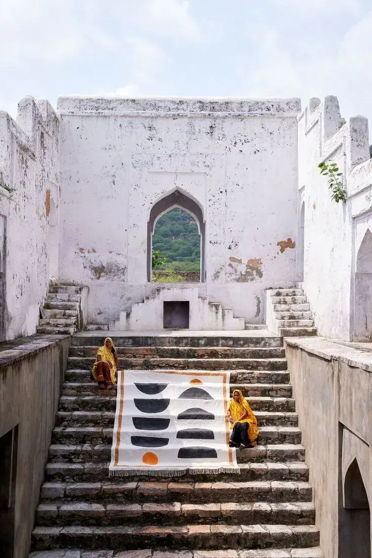 A graphic black, white and orange rug laid on stone steps with two people seated beside it