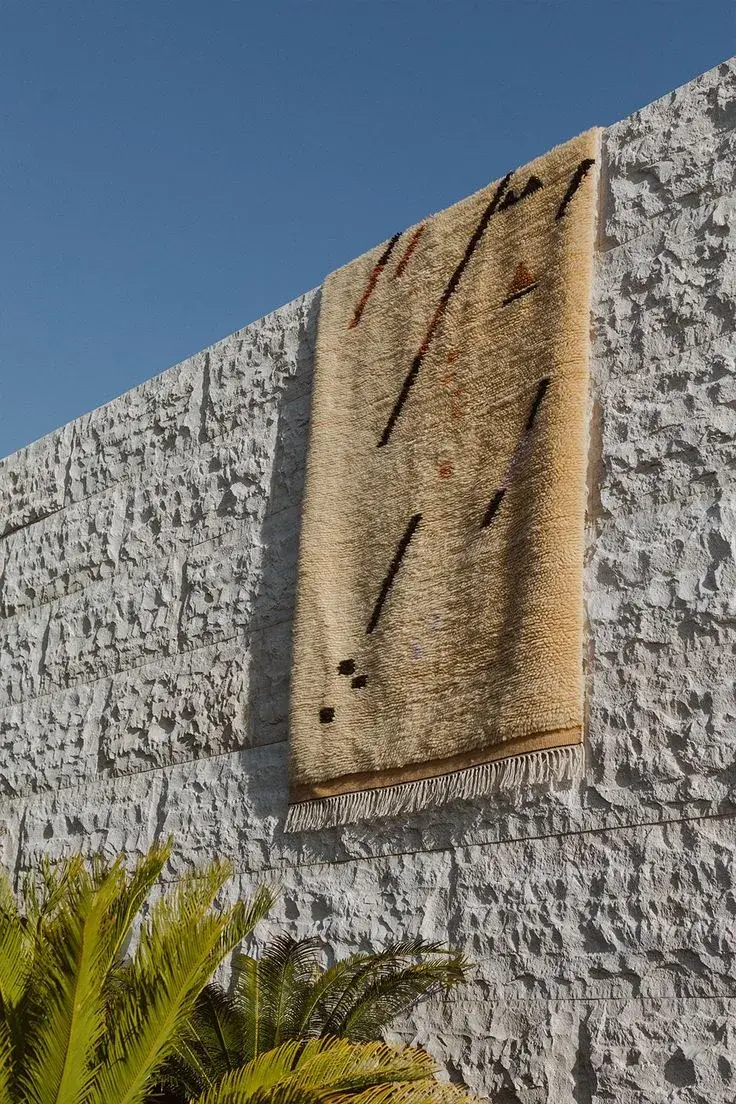 A beige rug with dark marks hung against a textured pale stone wall