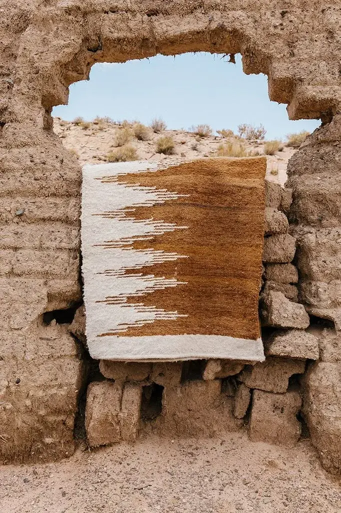A white and ochre rug hung in an opening in a weathered earth wall