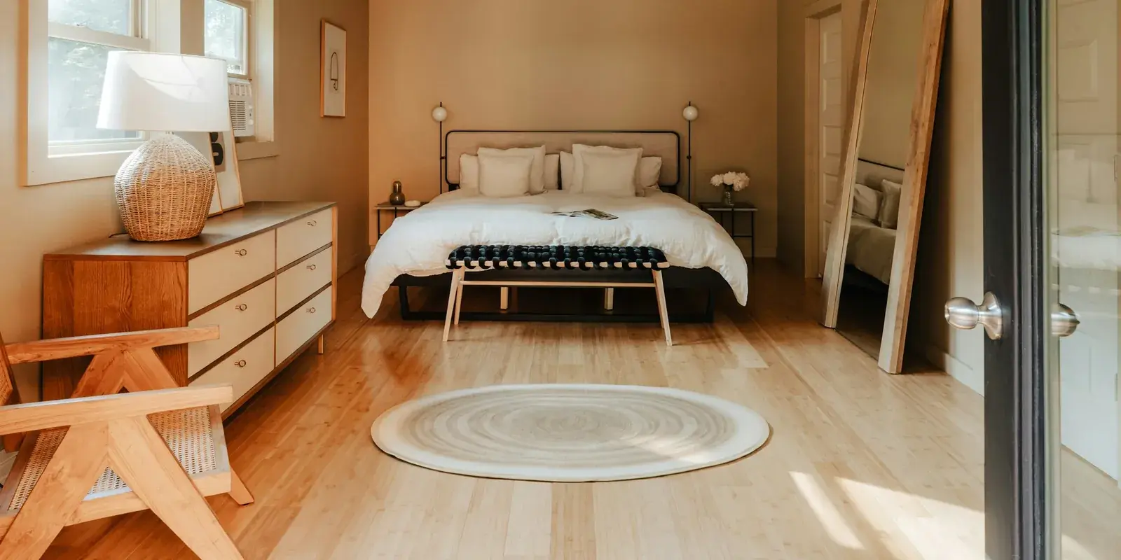 A sunlit bedroom with a round woven rug on a pale wood floor