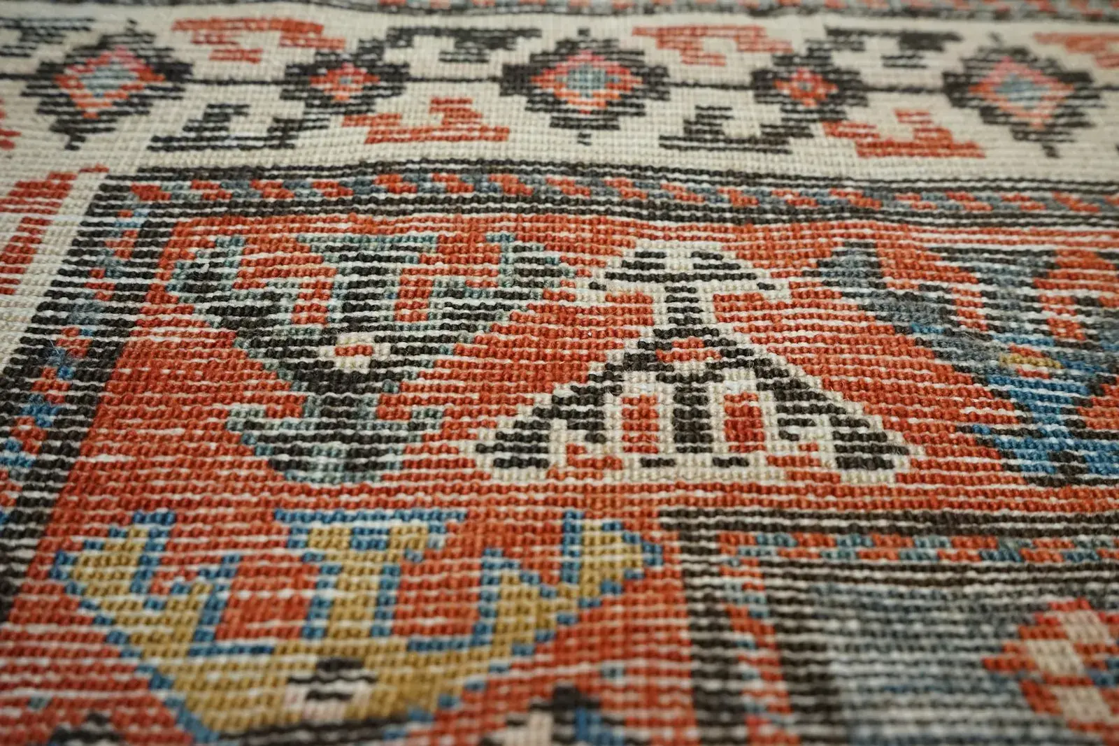 Close-up of a knotted wool rug in red, ivory and indigo with a geometric tribal-style border