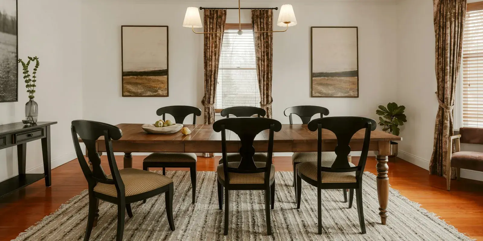 A dining room with a wooden table and black chairs on a striped flatweave rug