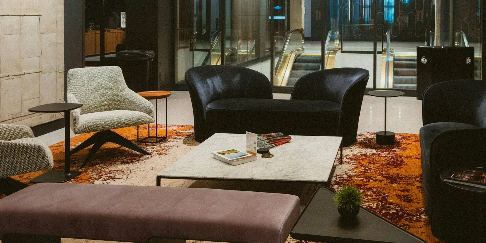 A hotel lobby seating area with armchairs and a marble table on a rust and cream rug