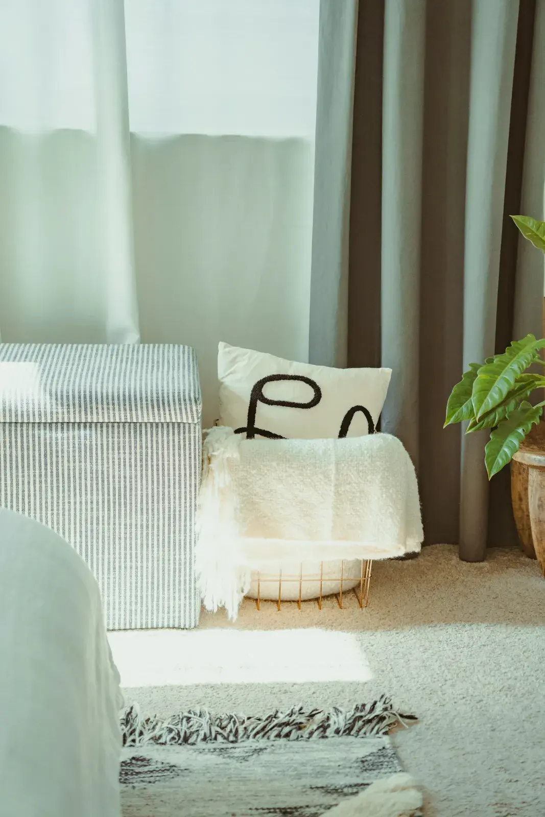 A striped storage ottoman in a bright bedroom with a graphic cushion and a cream throw resting on it
