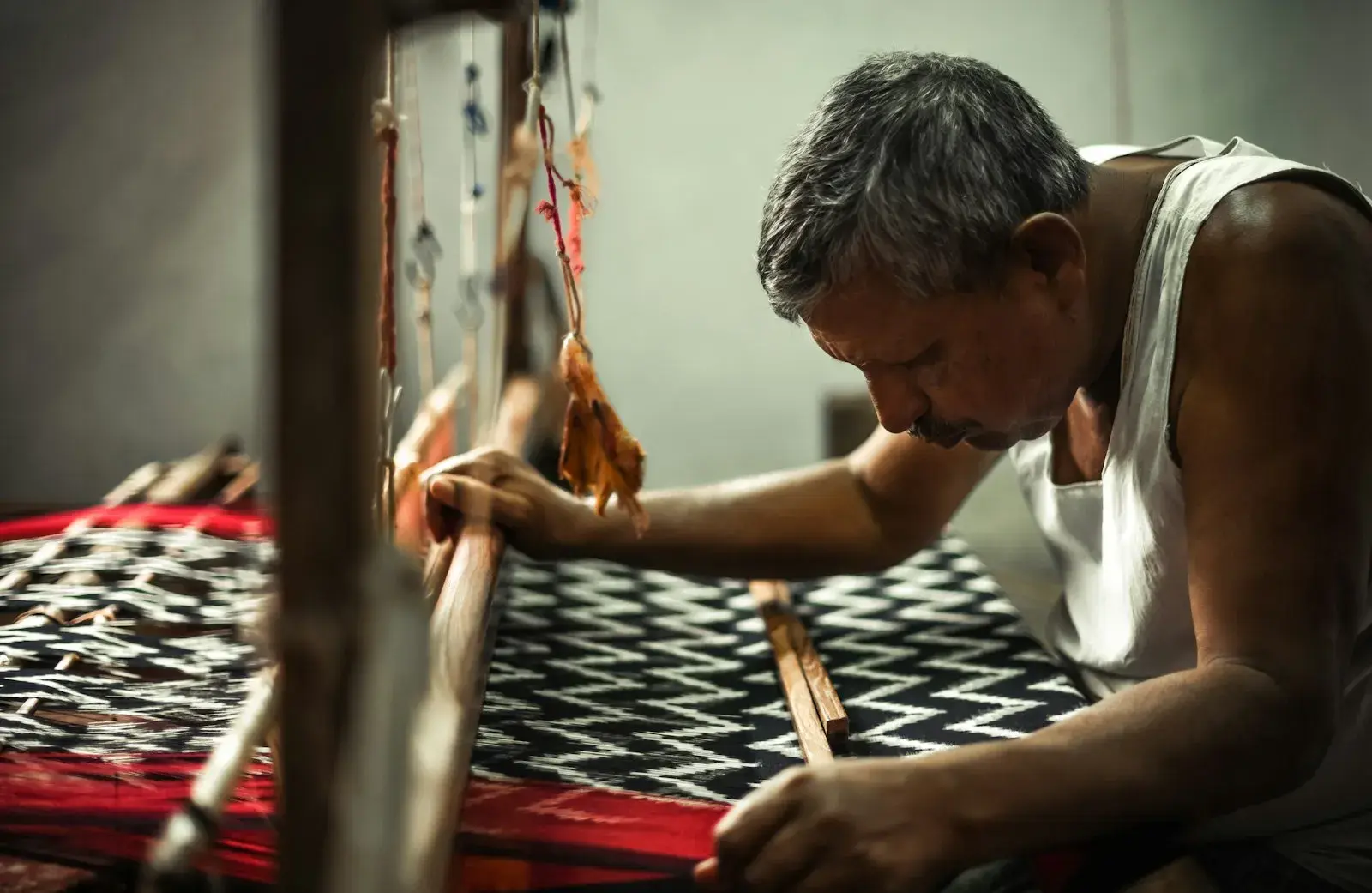 A weaver working at a handloom in Pochampally, India, shaping a black and white zigzag textile on red warp