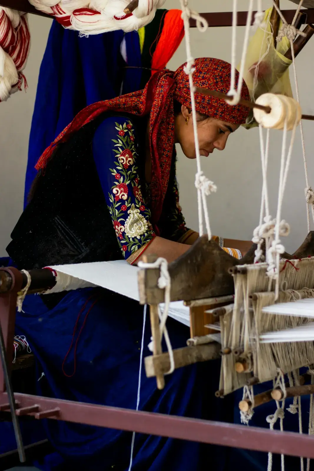 A weaver at a traditional hand loom with warp threads and heddles, the kind of loom used for flatwoven rugs