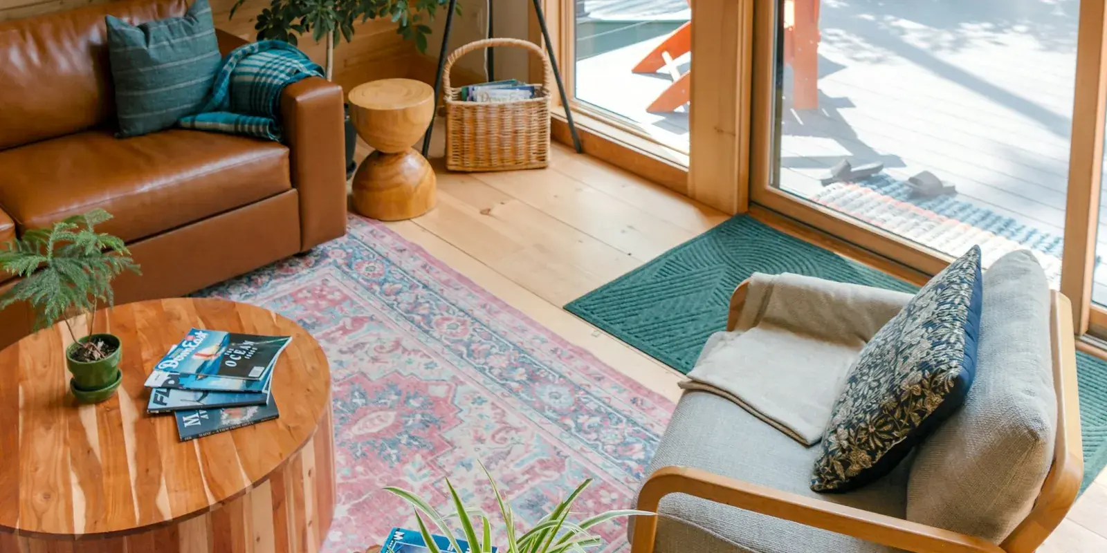 A timber cabin living room with a leather sofa, an armchair and a pink and blue patterned rug by a glass door