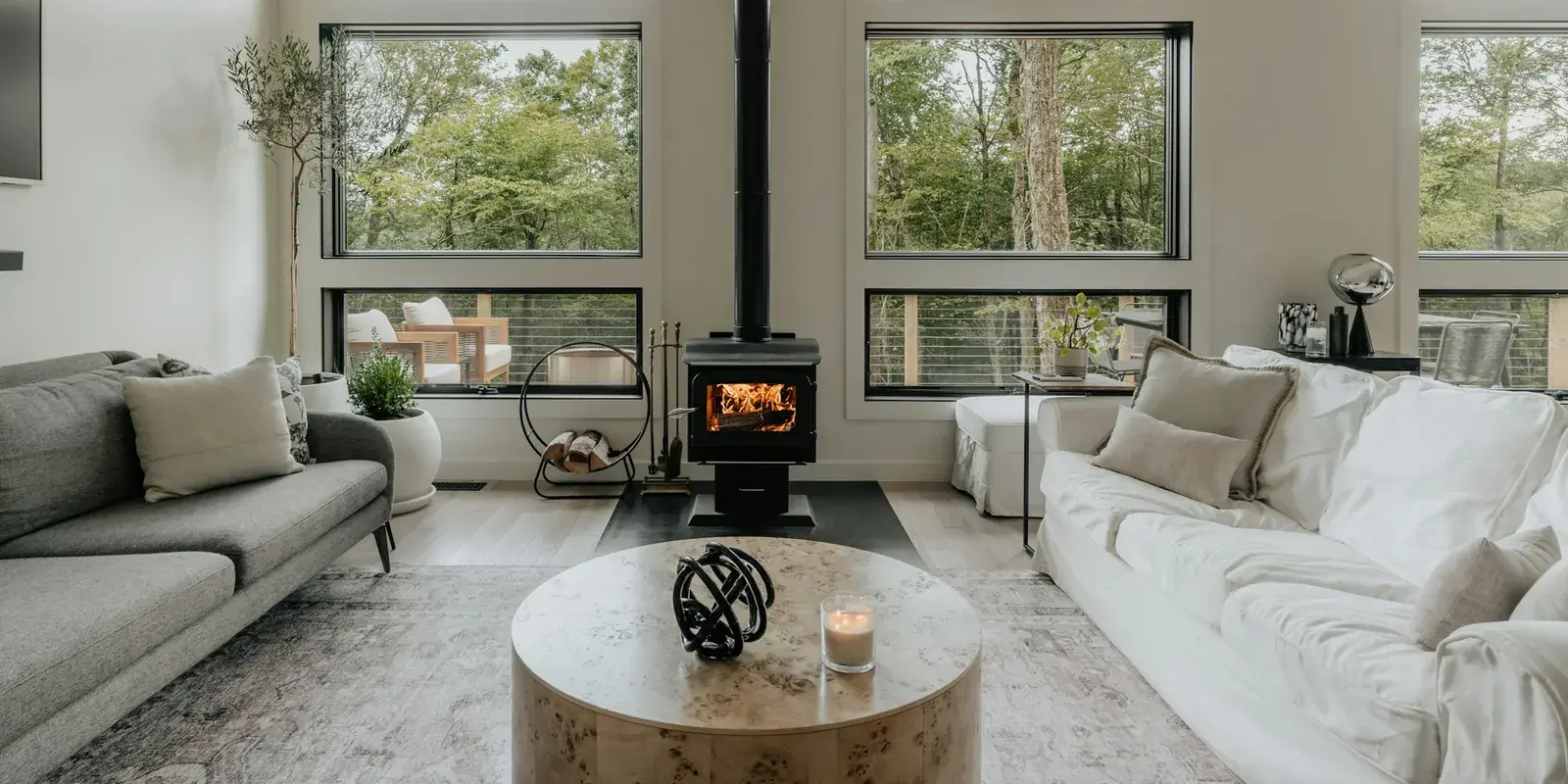 A minimalist living room with large windows, a wood stove, two sofas and a soft grey rug