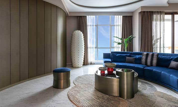 A hotel suite lounge with a round textured rug beneath a low table and curved sofa